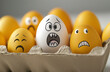 © Aleena  - A carton of eggs with various faces drawn on them, including one yellow egg and the rest white or brown.