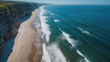 Canvas Print - Aerial view of coastline featuring waves crashing on sandy beach with cliffs in background under clear blue sky