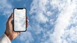 © lililia - Woman's hand holds a smartphone horizontally, capturing the moment with a vibrant blue sky blurred in the background