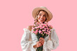 © HBS - Smiling happy dreamy girl in straw hat and trendy dress holding bouquet of pink carnations and looking aside while standing on pink background. Stylish young girl with delicate pink flowers.