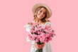 © HBS - Smiling happy young woman in a straw hat holding a bouquet of pink flowers, radiating happiness and spring vibes against a pastel pink background. Springtime and International women's day.