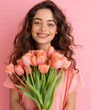 © AltisArt - Smiling Young Woman with Curly Hair Holding Pink Tulips on Pink Background