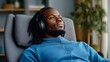 © Raul - Young Black man relaxes in a comfortable chair, listening to music with headphones. Serene atmosphere, blue tones.