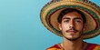 © Georg - Young man wearing a colorful sombrero posing against a bright blue background during a festive celebration