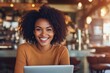 © Dmitrii - Young woman smiles at the camera while working on a laptop in a cozy cafe during the morning hours