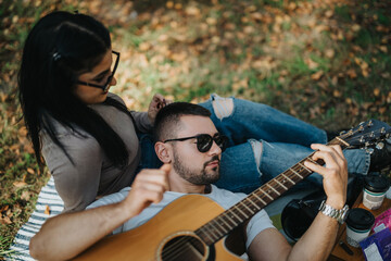 Poster - A young couple relaxes outdoors, enjoying each other's company with soothing guitar music. The serene setting enhances their connection and peaceful vibe, surrounded by nature in casual attire.