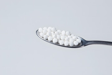 Wall Mural - Spoonful of Tiny White Pills: Close-up of a spoon filled with numerous small, white, round pills against a minimalist, bright backdrop.