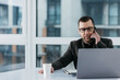 © Валерия Стоганенко - Middle aged caucasian business manager ceo using cell phone mobile app, laptop. Focused mature man businessman holding smartphone sit in office working online on gadget with copy space.