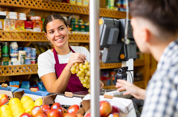 Wall Mural - Friendly saleswoman serving a guy customer in a store weighs grapes on a scale