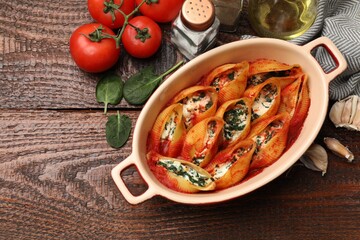 Wall Mural - Delicious conchiglie pasta with ricotta cheese, spinach and tomato sauce in baking dish on wooden table, flat lay. Space for text