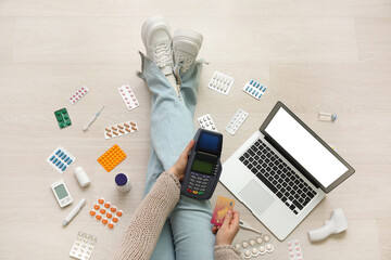 Wall Mural - Young woman with payment terminal, credit card, modern laptop and medicines sitting on floor