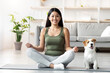 © Prostock-studio - Athletic asian young woman doing yoga with her adorable loyal red and white doggy at home, chinese lady sitting in lotus pose, jack russel puppy sitting by owner on fitness mat, copy space