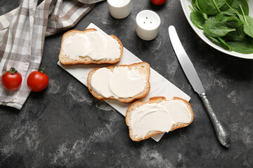 Wall Mural - Board of tasty bruschetta with processed cheese, spinach leaves and fresh tomatoes on black background. Top view