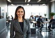 © 정아 강 - Mujer hispana en traje sonriendo en un espacio de oficinas moderno. Los empleados están trabajando en la oficina