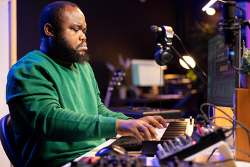 Leinwandbilder - African american audio technician using piano synthesizer keys to add audio effects in post production, editing tunes with digital software and mixing console. Male artist in home studio.
