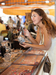 Wall Mural - Satisfied interested young woman choosing interesting antique things at traditional flea market