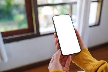 Wall Mural - Mockup image of a woman holding mobile phone with blank desktop screen while sitting in bed room at home