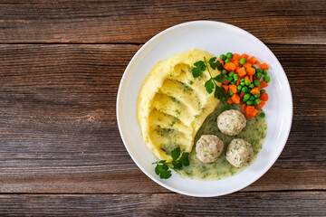 Wall Mural - Boiled meatballs in dill sauce with mashed potatoes and boiled carrot and green peas on wooden table	