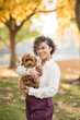 © Cavan - Smiling woman holding her fluffy dog in a beautiful autumn park