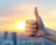 © Nuth - Close-up of a hand showing thumbs up against a bright, blurred sunset background, symbolizing positivity, approval, and success.