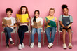© Prostock-studio - Multinational kids with textbooks and copybooks sitting on chairs and looking at camera against pink background