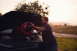 © Johnér - Man keeping power cable in car hood at sunset