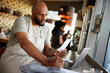 © Johnér - Male owner with shaved head examining financial bills while working at cafe