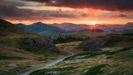 Wall Mural - Serene sunset over rolling hills with winding path, warm orange and muted blue tones under a dramatic sky with scattered clouds.