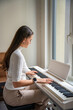 © dtatiana - Young woman playing on white piano synthesizer at home. Concept of home lesson of music: learning music enhances motor skills, hearing, and intelligence, fostering creativity