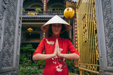 Wall Mural - woman traveler tourist in a Vietnamese hat prays at a Buddhist temple on pagoda in Hoi An in Vietnam in Asia