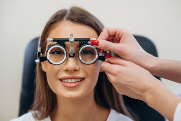 Wall Mural - Positive facial expression. Young woman is checking her vision in the ophthalmologist cabinet