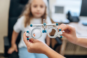 Wall Mural - Showing and holding device for measuring sight sharpness. Little girl at the ophthalmologist clinic with doctor