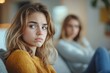 © Shaila - Annoyed mother gesturing to teen daughter sitting on couch, sad teen girl looking away, relationship problems with teenagers and generation gap, Generative AI