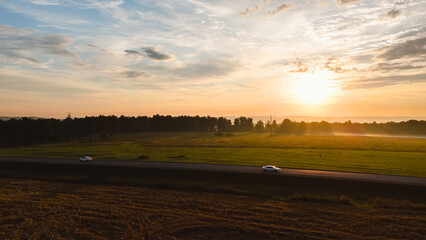 Wall Mural - dawn in a wheat field, a car is driving along the highway, fog is creeping on the horizon