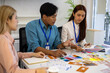 © Somdetmeaow - Three people are sitting around a table, working on a project. They are wearing name tags and are pointing at a whiteboard. Scene is collaborative and focused