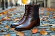 © whitestorm - Elegant brown leather Chelsea boots on cobblestone street covered with autumn leaves, capturing the essence of fall fashion and urban style with blurred background.