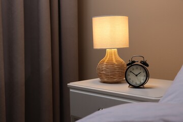 Wall Mural - Glowing lamp and alarm clock on nightstand in bedroom. Space for text