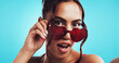 © peopleimages.com - Selfie, woman and heart sunglasses for fashion, pov or social media on blue studio background. Portrait, shades or girl with cool accessory, love or stylish influencer post photography for valentines
