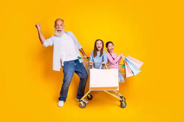 Poster - Elderly man and two girls joyfully posing in a shopping cart with vibrant yellow background