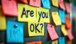 © Arthur Woods - Colorful sticky notes on corkboard. One note says Okay Workplace mental health initiative. Employee support. Caring, encouraging work environment. Positive message for colleagues. Promoting