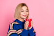 © deagreez - Young woman smiling with a red mug against a pink background, wearing a stylish striped sweater for lifestyle and advertising concepts.