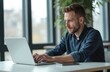 © Vadym - Man works at laptop in office. Businessman using computer, browsing internet. Caucasian male with beard types on keyboard. Modern workplace. Remote work at home. Side view, close-up shot.