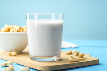 Wall Mural - Fresh cashew milk in glass and nuts on light blue wooden table, closeup