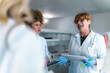© DusanJelicic - Senior professor wearing a lab coat and gloves, holding a tablet while explaining complex lessons to a diverse group of students in a university laboratory setting