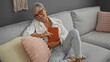 © Krakenimages.com - Beautiful mature woman with grey hair relaxing in her living room, holding a book, sitting on a couch, enjoying a peaceful moment indoors at home.
