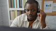 © Krakenimages.com - Young, black, man wearing a headset working in an office environment, focusing intently at his computer screen.