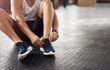 © peopleimages.com - Feet, gym and shoelaces for training on floor with start, routine and sneakers for fitness in morning. Person, hands and legs with shoes for workout, wellness and ready with exercise at health club