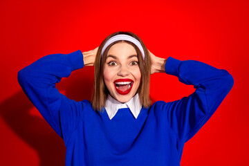 Wall Mural - Smiling woman wearing blue jumper with cheerful expression and headband on vibrant red background