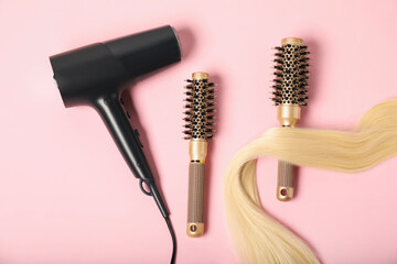 Wall Mural - Stylish round brushes, lock of blonde hair and hairdryer on pink background, flat lay