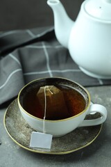 Wall Mural - Tea bag in cup with hot drink and teapot on gray textured table, closeup